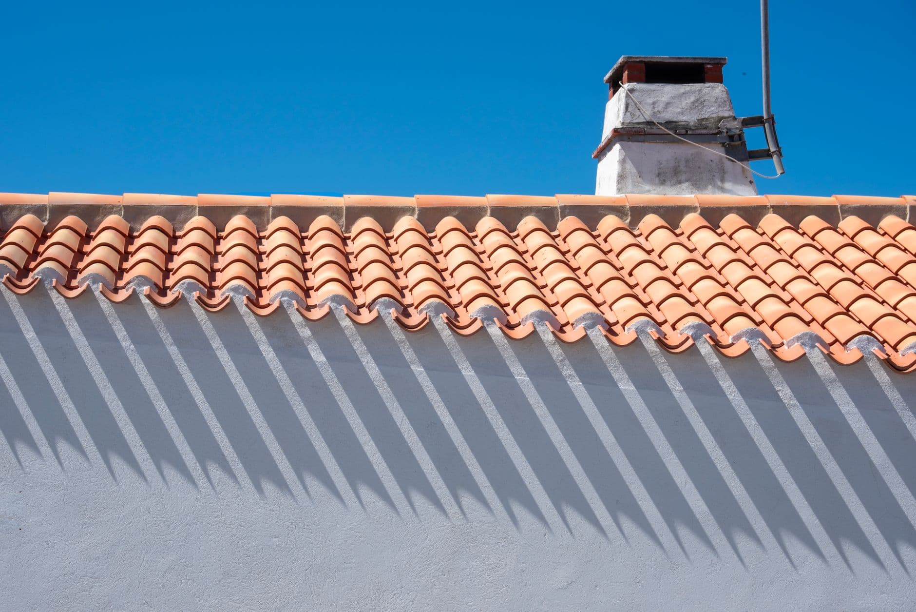 Orange roof tiles and chimney casting long shadows under a bright blue sky.