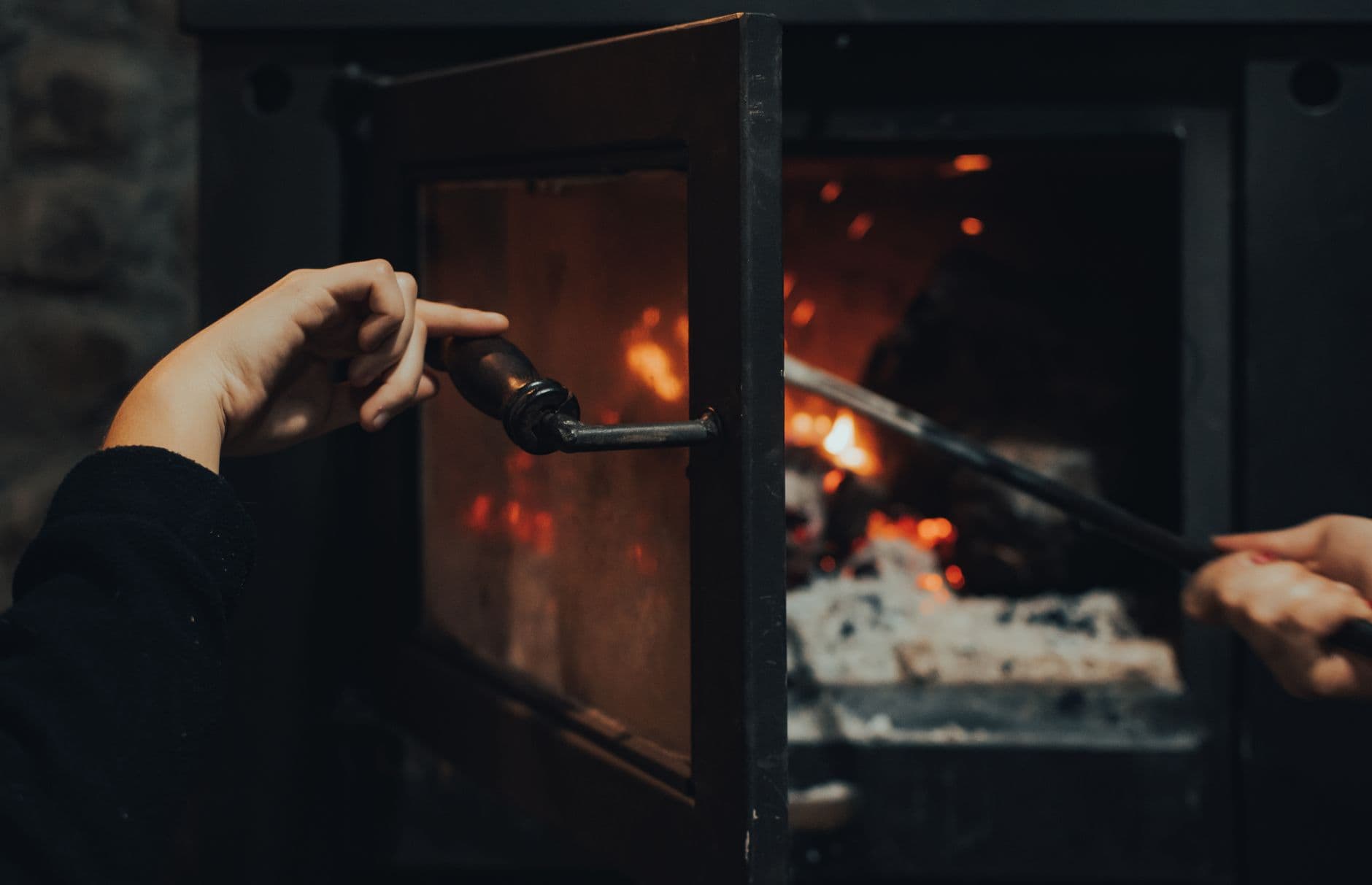 Close-up of hands opening and maintaining a warm fireplace for a cozy indoor setting.